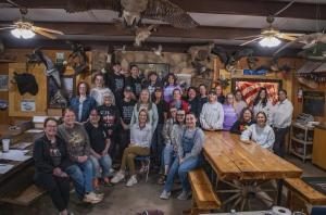 A large group inside the lodge dining hall with mounted trophies and wood-paneled walls